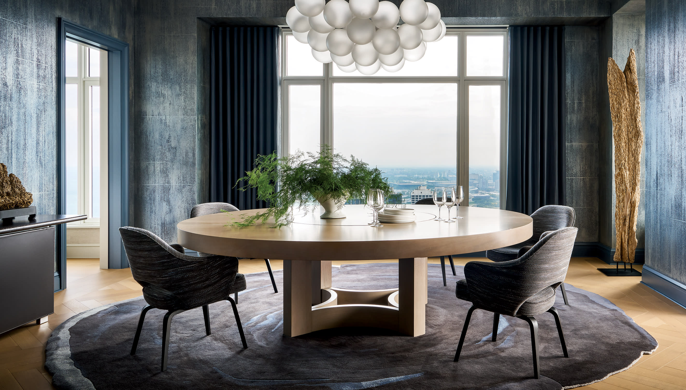 Luxury Interior Design Dining Room With Large Windows And With Blue Walls And With A Round Wood Dining Table And With Dark Blue Dining Chairs And With A Grey Round Rug